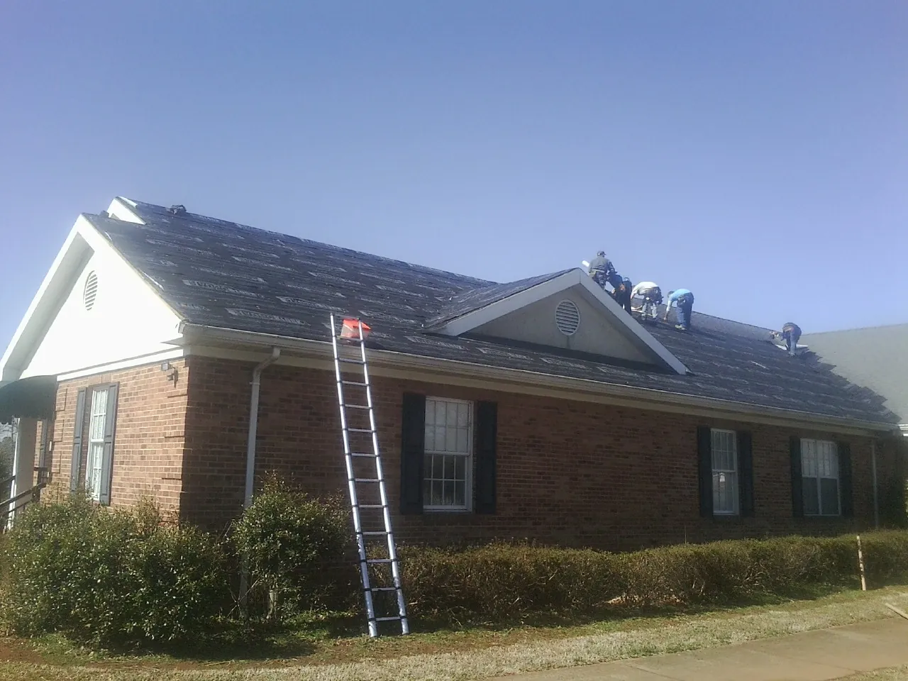 Crew tearing shingles off a brick ranch roof with a ladder set — Emergency Roof Repair work by our crew in North Branford