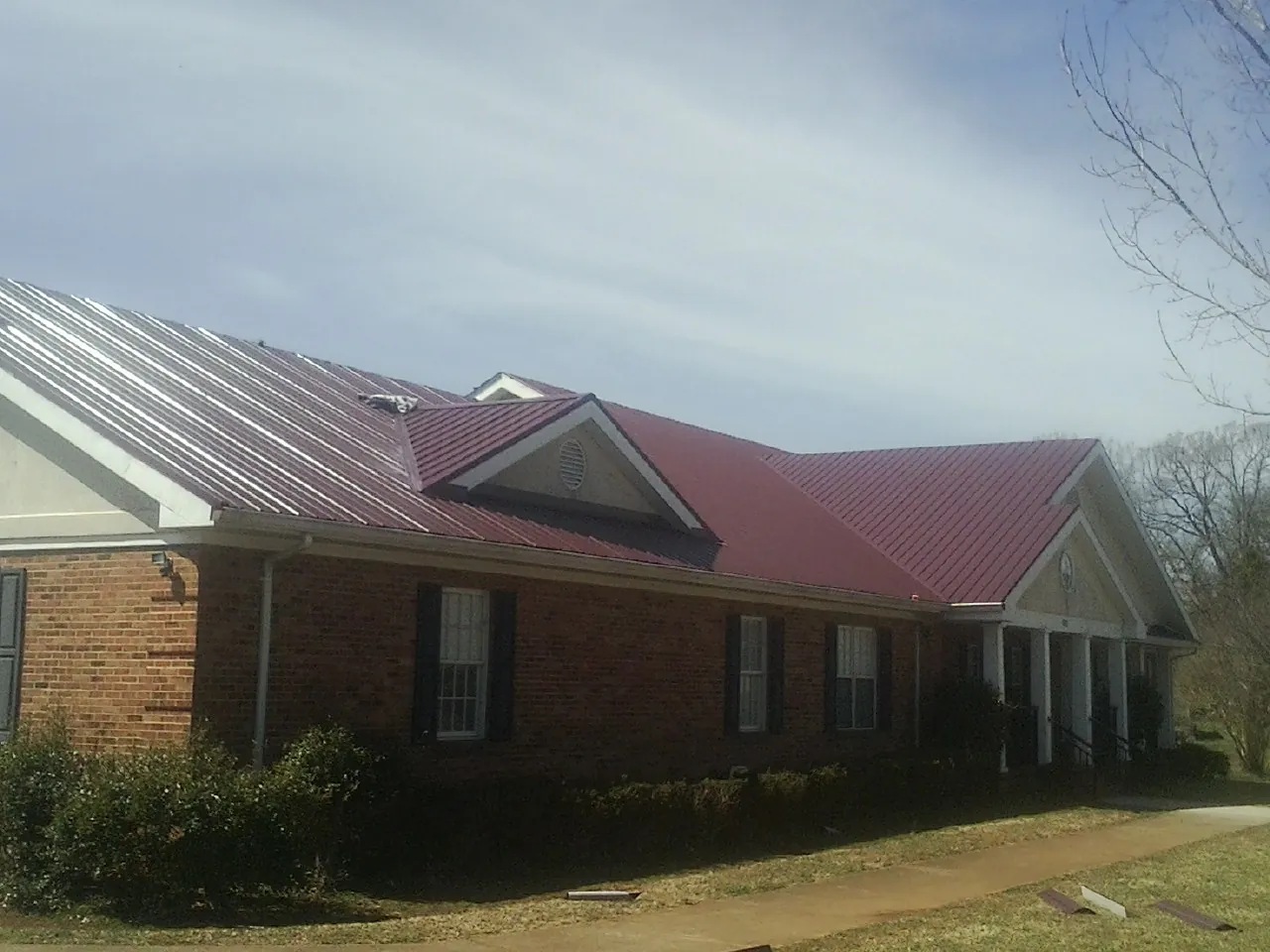Red metal roof with gabled entries on a long brick building, from a Hail Damage Roof Repair job in North Branford