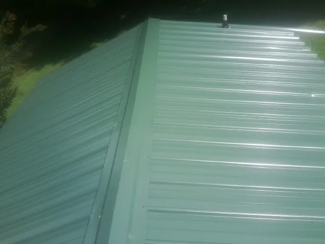 New green metal panels meeting at the ridge of a roof — Flat Roof Repair work by our crew in North Branford
