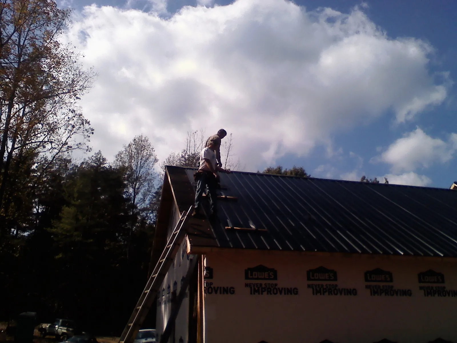 Roofer fastening dark metal panels high against a cloudy sky, from a Roof Inspection job in North Branford