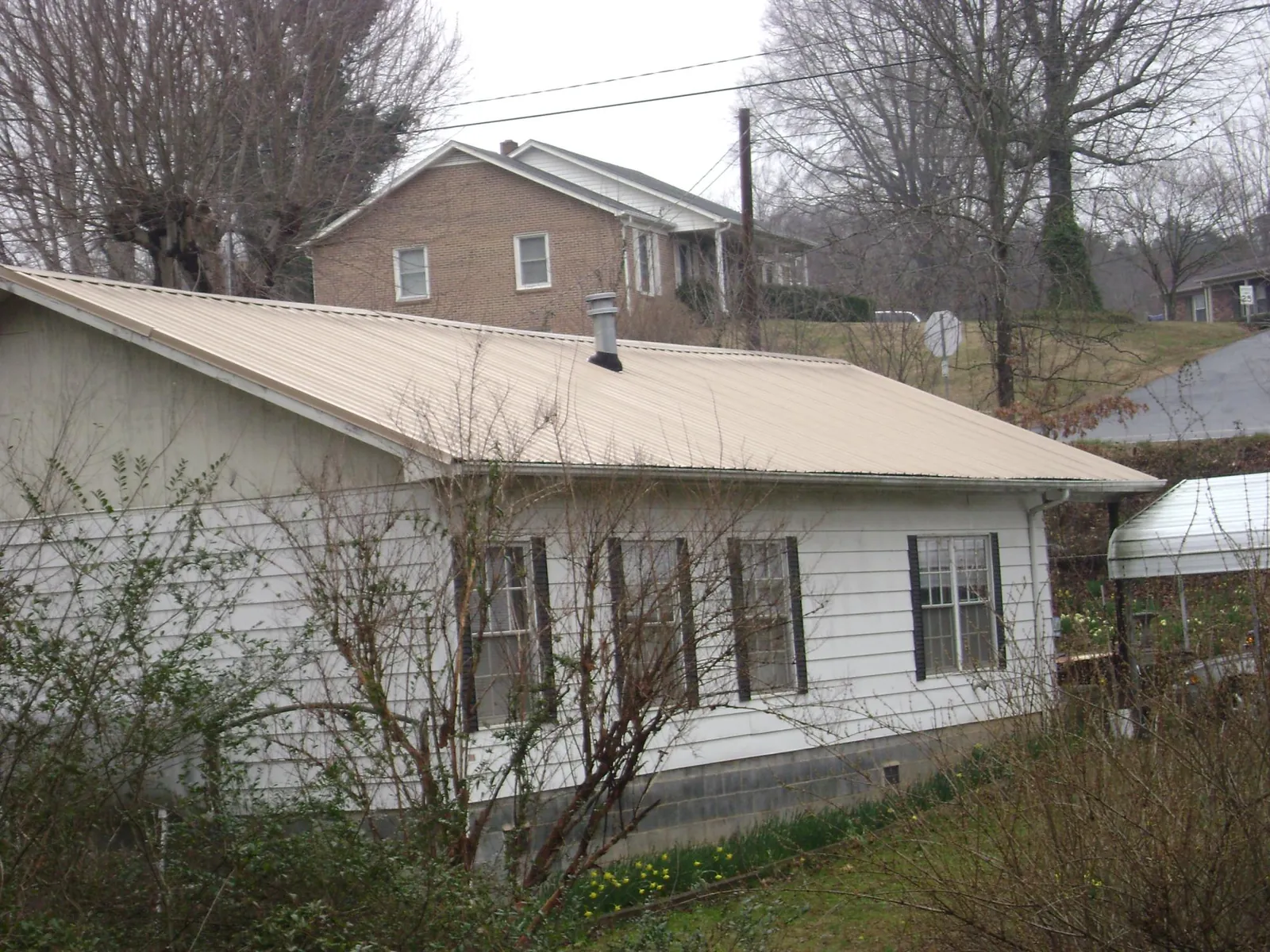 Tan metal roof on a white sided house set into a hillside — Commercial Roofing by Roofing Brothers in North Branford